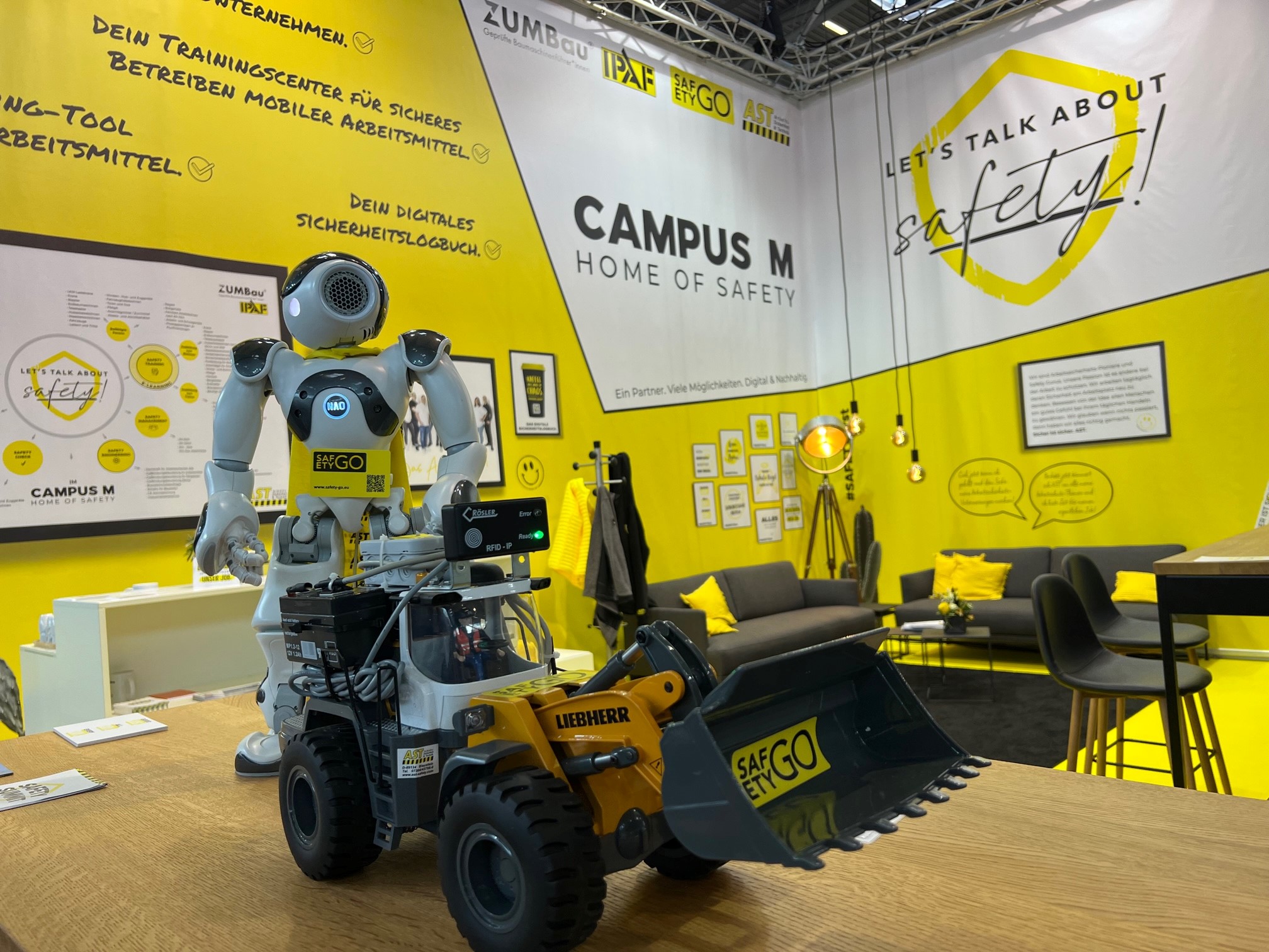 Messeauftritt mit Roboter Nao. Die SafetyGO GmbH & Co. KG und die AST Arbeitssicherheit und Technik GmbH präsentierten auf der bauma 2022 auf einem in auffallend Gelb gehaltenen Stand gemeinsam digitale Angebote.