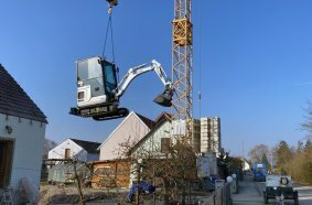Ein spektakuläres Bild zeigt, wie der brandneue Minibagger auf einer aktuellen Baustelle per Kran in seinen Einsatzbereich gehoben wird – ein beeindruckender Start in seine Karriere bei der EHTA GmbH.