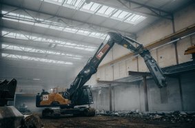Abbruchbagger mit Erdbauausrüstung und ausgefahrenem Teleskopfahrwerk im Gebäude