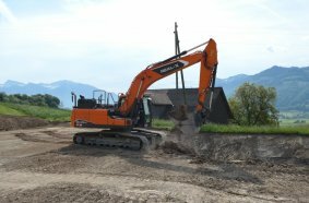 Prächtige Kulisse: Der autonom arbeitende DEVELON-Real-X-Kettenbagger DX225LC beim Praxiseinsatz im ehemaligen Steinbruch der KIBAG im schweizerischen Tuggen. 