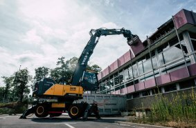 Der Volvo-Umschlagbagger EW240 Electric MH reißt die ersten Panele vom Gebäude ab.