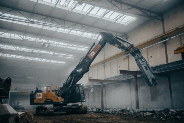 Abbruchbagger mit Erdbauausrüstung und ausgefahrenem Teleskopfahrwerk im Gebäude