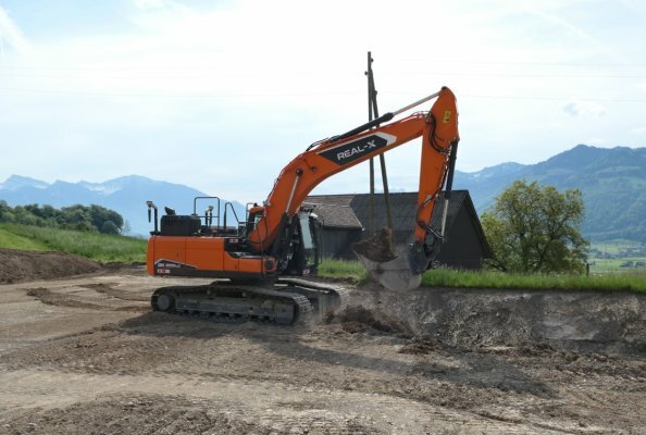 Prächtige Kulisse: Der autonom arbeitende DEVELON-Real-X-Kettenbagger DX225LC beim Praxiseinsatz im ehemaligen Steinbruch der KIBAG im schweizerischen Tuggen. 